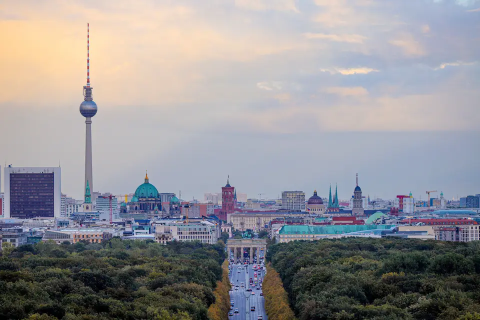 Tiergarten'ın ağaçları arasından uzanan cadde, Brandenburg Kapısı ve arkada Televizyon Kulesi ile Berlin silueti