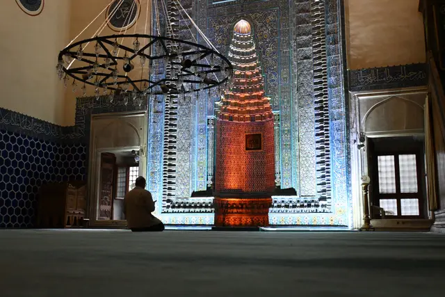 Yeşil Cami'nin çinili mihrabı ve avizesi; önünde arkası dönük namaz kılan bir kişi